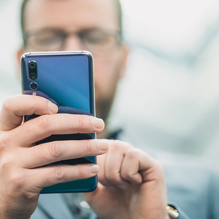 Mann surft online am Smartphone großes Firmengebauede im Hintergrund