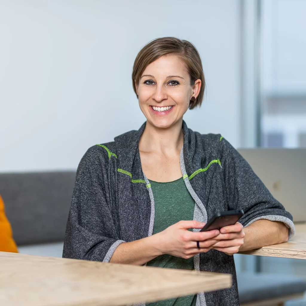 Frau in Business-Outfit sitzt am Schreibtisch und lächelt in die Kamera